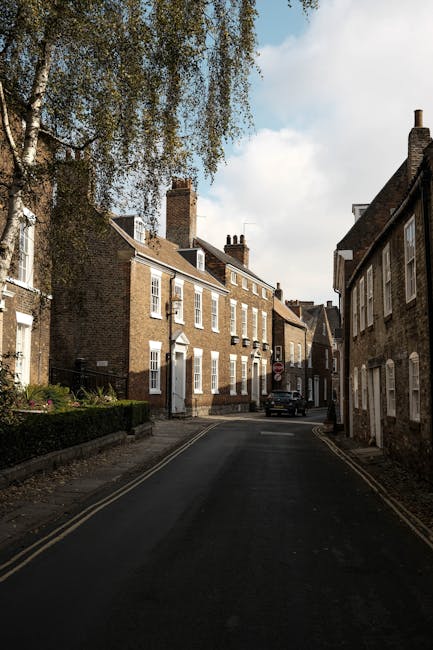 A narrow residential street in New Barnet with brick terraced houses on both sides, some with white window frames and chimneys visible on the rooftops. The street is paved with dark asphalt and featur